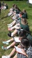 children sitting in a row outside holding clipboards