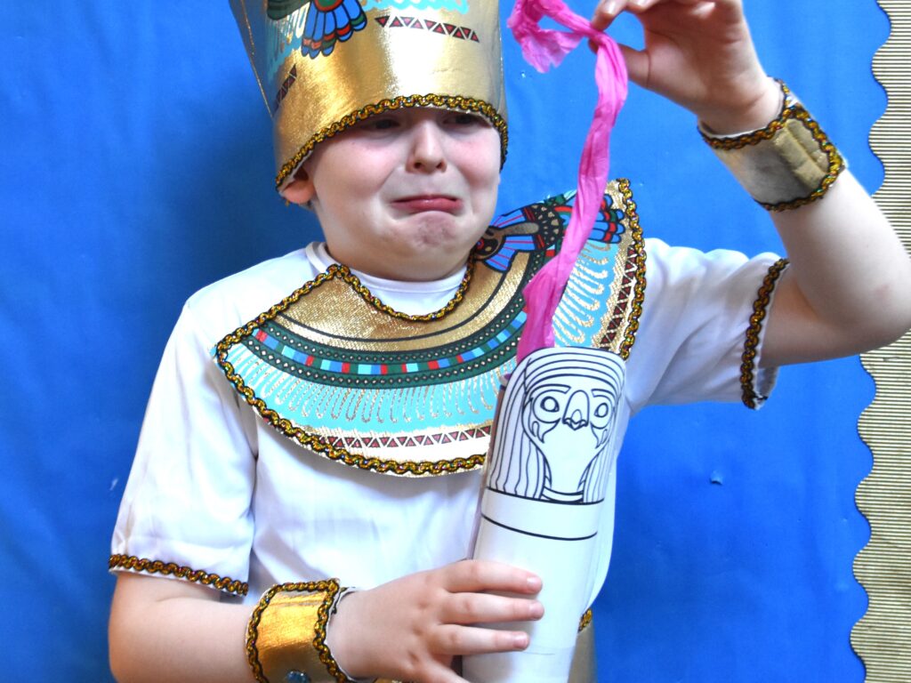 student dressed as an Egyptian pulling out tissue paper from a made urn