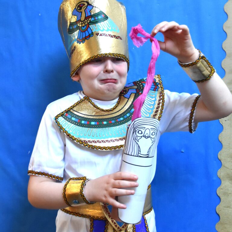 student dressed as an Egyptian pulling out tissue paper from a made urn